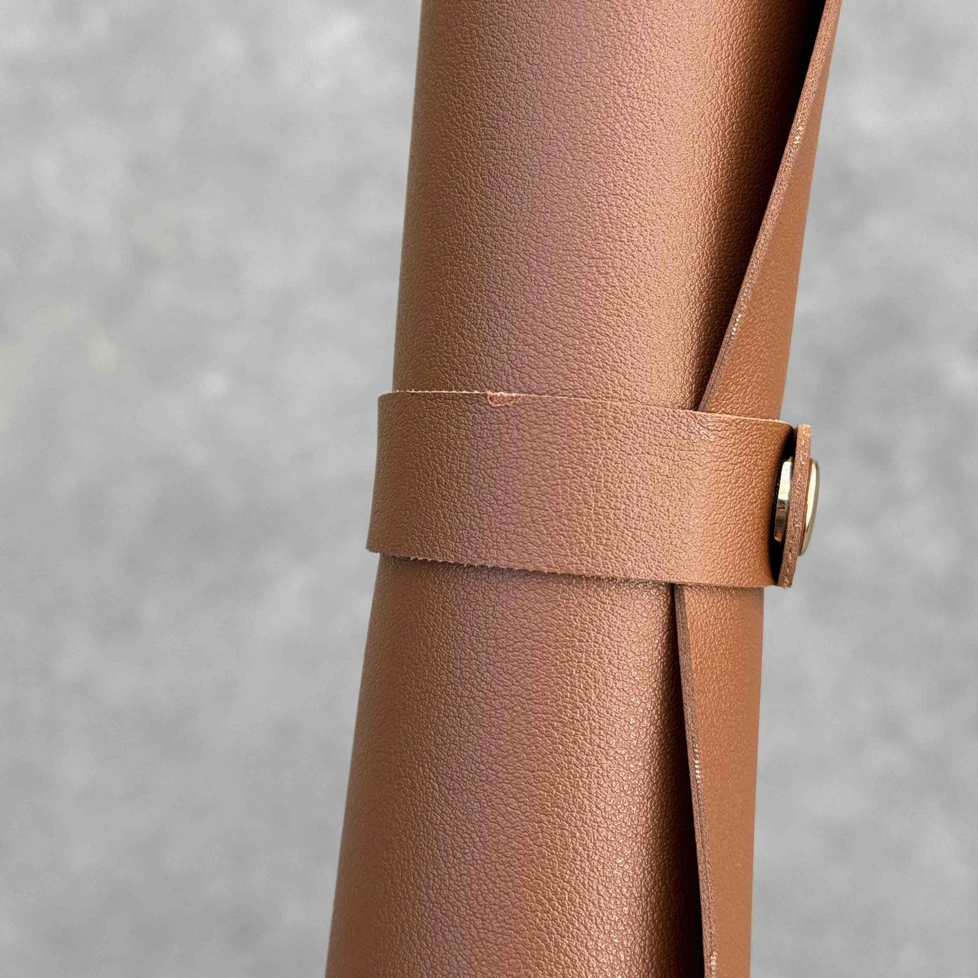 Gros plan sur un tapis de rempotage en simili cuir marron enroulé et maintenu par une bande avec bouton doré