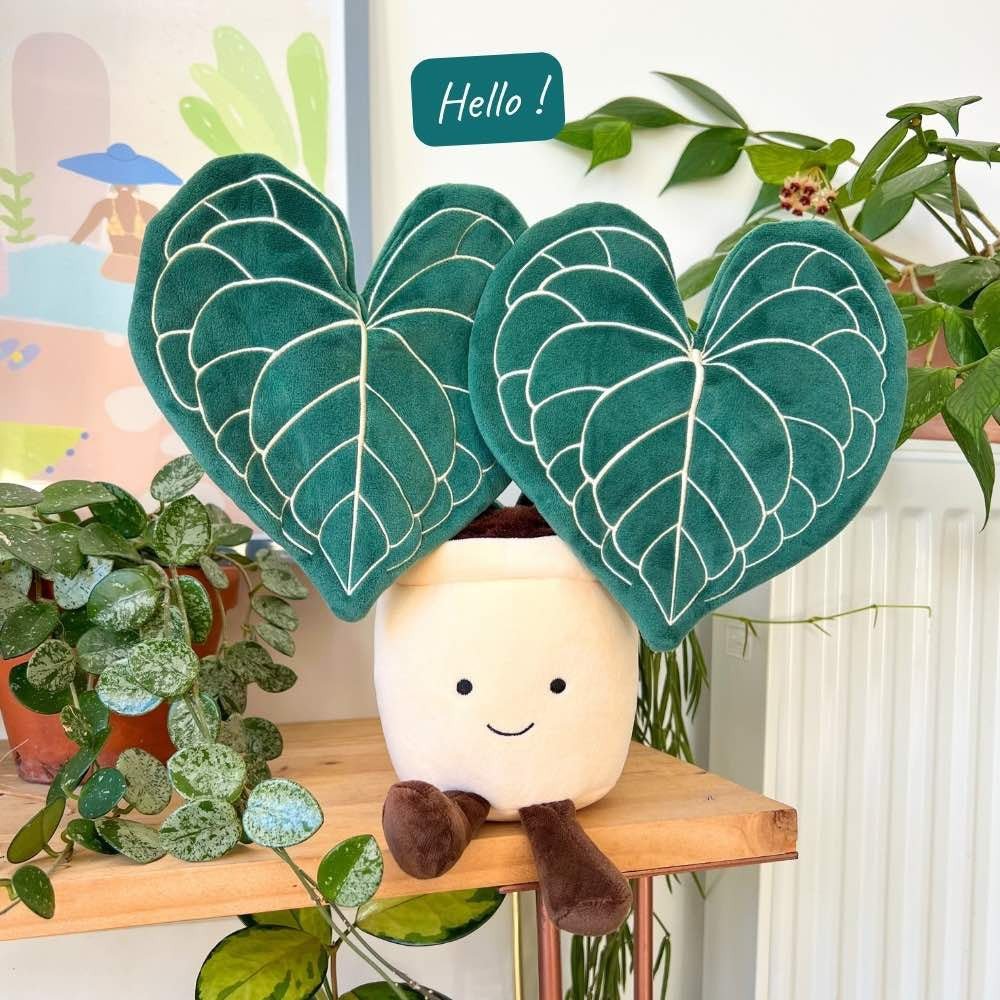 La peluche Clari est une mascotte adorable avec un pot beige souriant et de grandes feuilles vertes aux nervures blanches