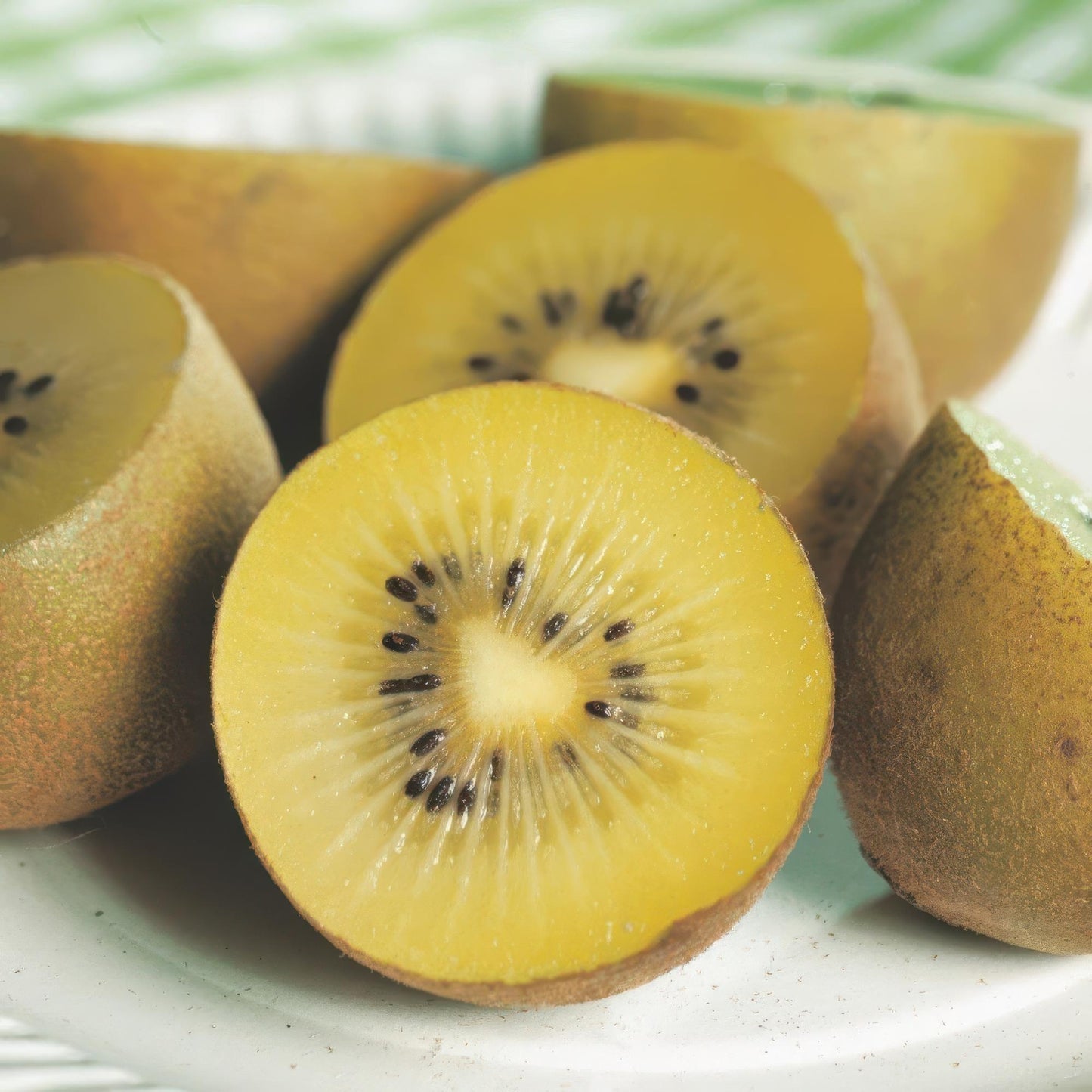 Actinidia deliciosa Golden Kiwi. Gros plan de kiwis à chair jaune, coupés en deux, révélant les graines noires sur un fond clair.