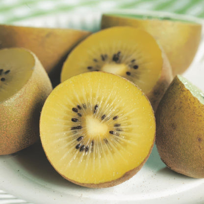Actinidia deliciosa Golden Kiwi. Gros plan de kiwis à chair jaune, coupés en deux, révélant les graines noires sur un fond clair.