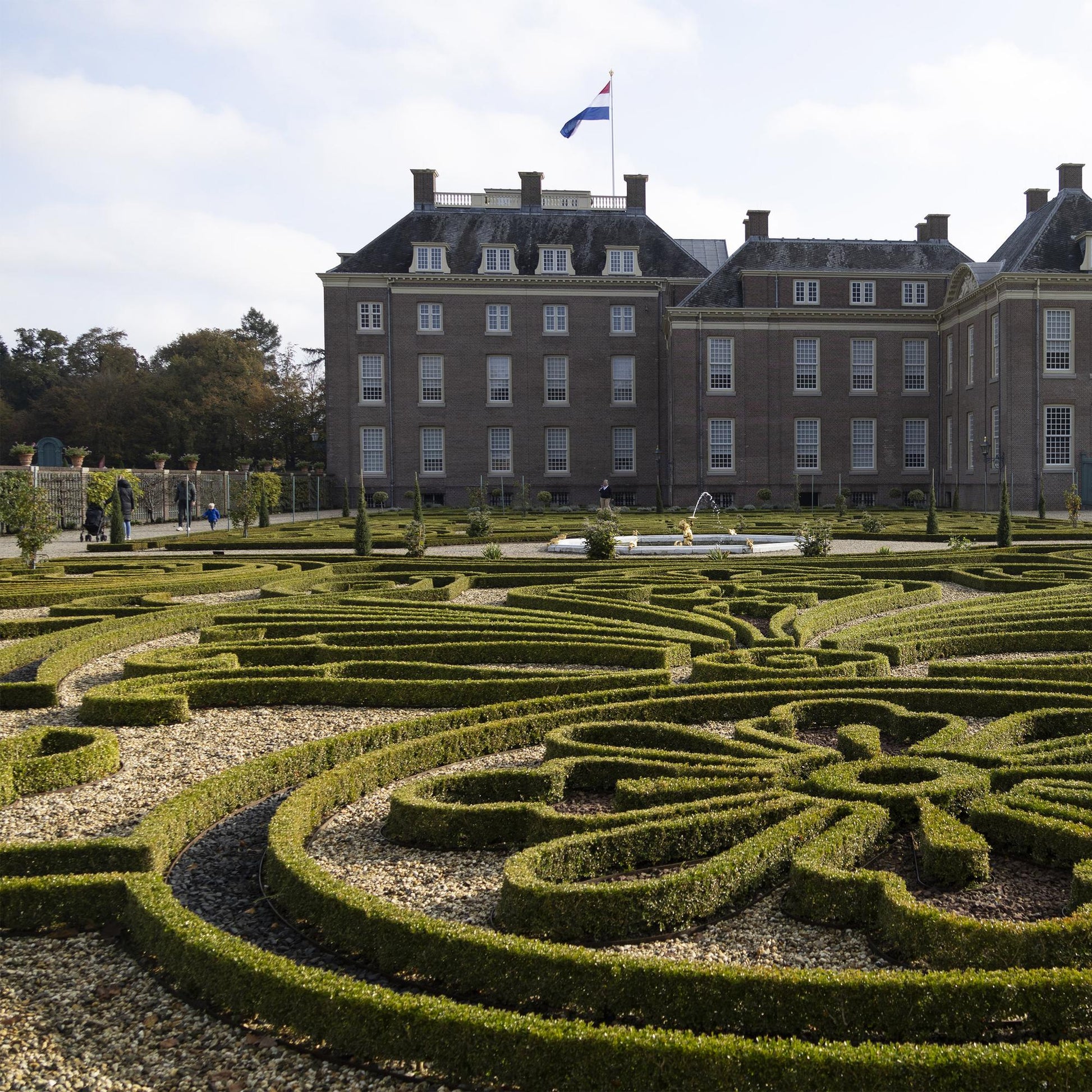 Buxus Babylon Beauty. Jardin à la française avec des parterres de buis taillés en motifs complexes devant un grand bâtiment historique en br