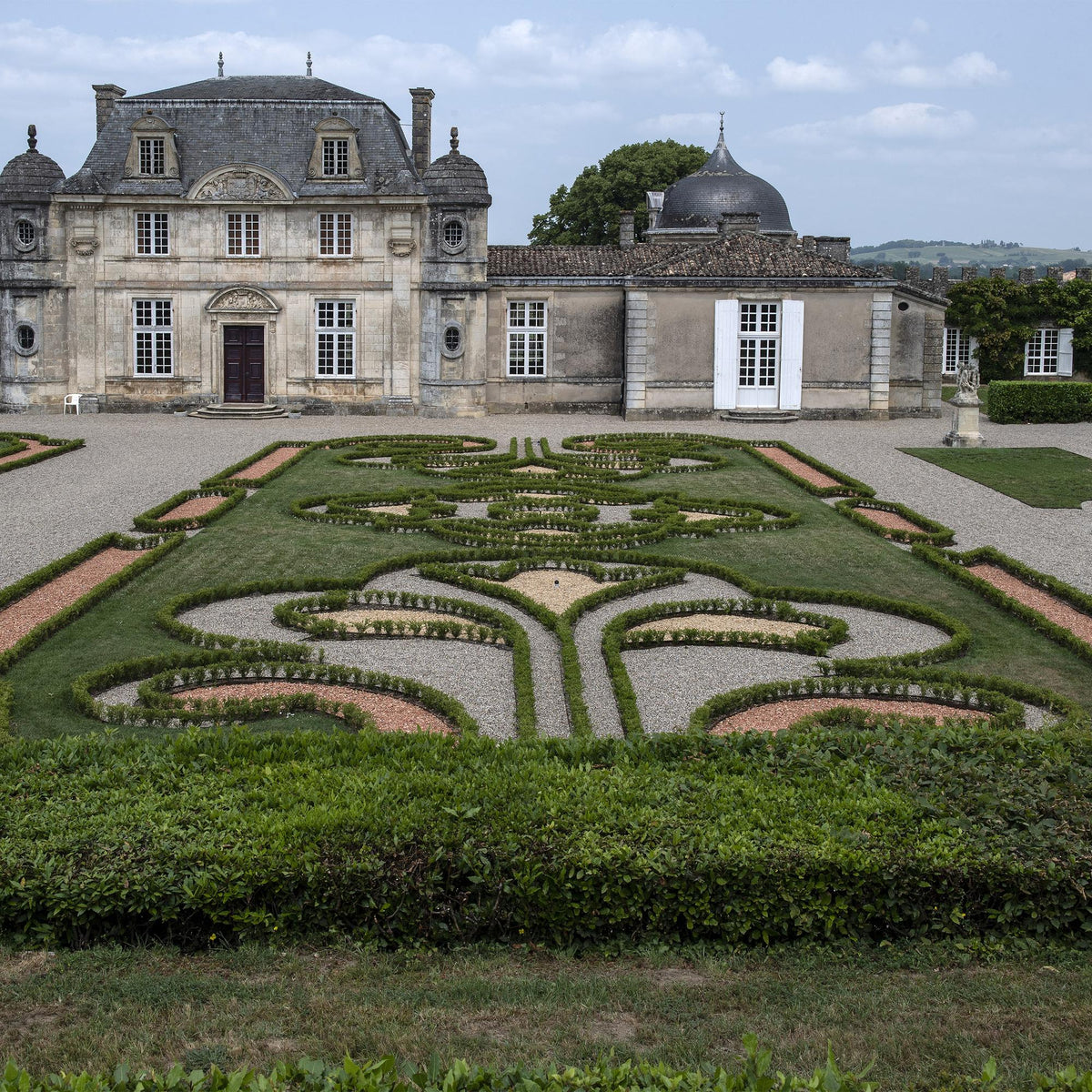 Buxus BetterBuxus Babylon Beauty, haie taillée en bordure d'un parterre de jardin à la française, devant un château classique.